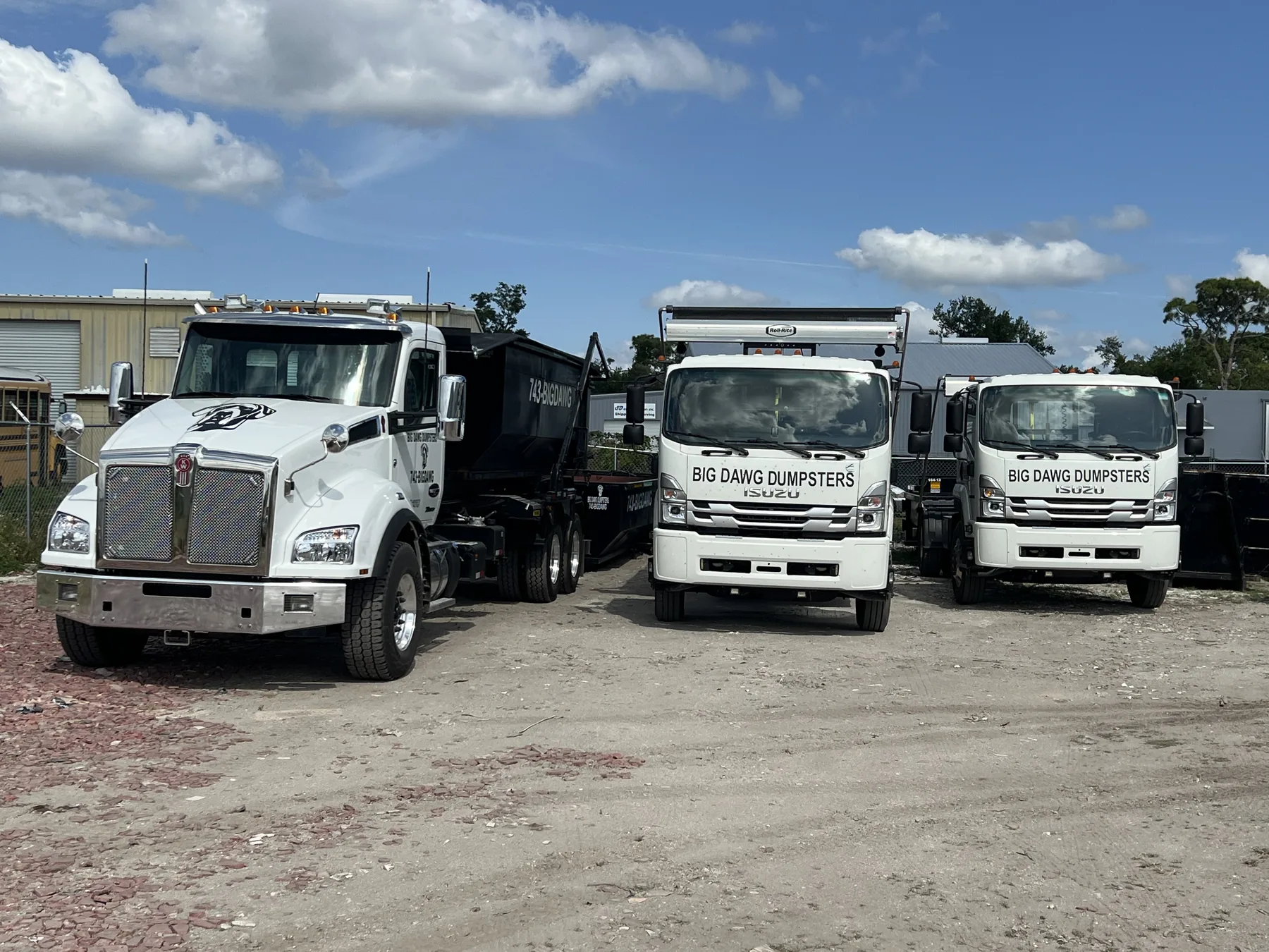 Three white Big Dawg Dumpsters roll-off trucks parked with black containers at the Port Charlotte fleet yard.