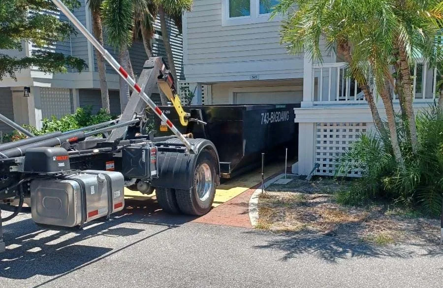 A Big Dawg roll-off truck placing a black dumpster in a paved Southwest Florida residential driveway.